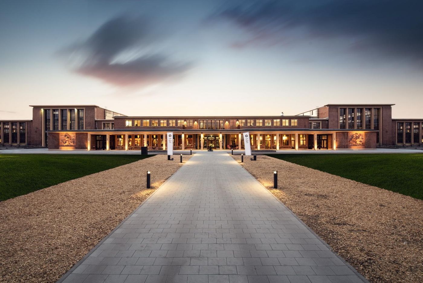 Brick building of the Drivers & Business Club Munich at dusk, with a lit path in front